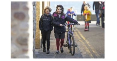 2 girls, one pushing a bike, walking on a pavement