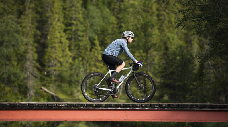 Side on shot of Emmie Collinge riding a gravel bike across bridge