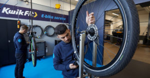 Bicycle wheel being trued in front of KwikFit e-bike sign 
