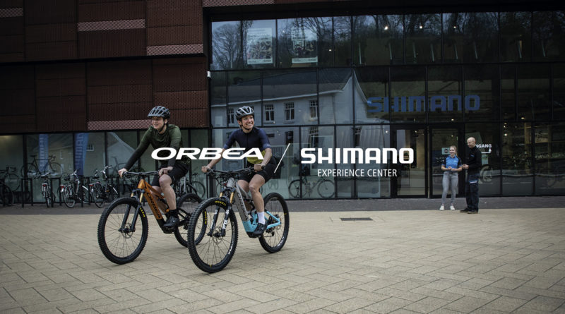 Shimano service centre in the background and 2 cyclists on Orbea bikes in the foreground