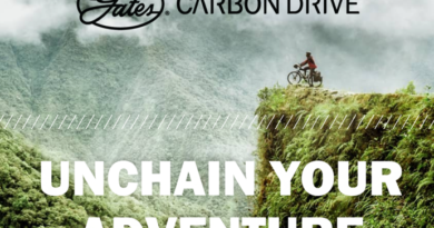 Lush, green, mountains in low cloud, with cyclist on cliff edge looking out over the vista - Gates Carbon Drive 'Unchain your adventure' text at top and bottom of image