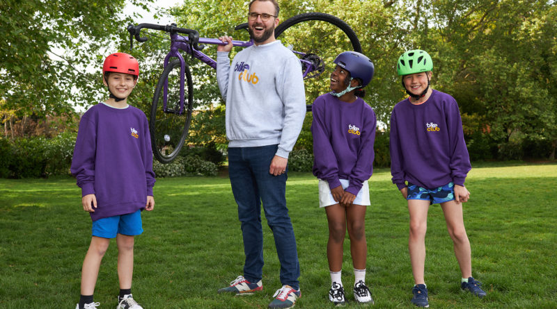 Bike Club Co Founder James Symes holds bike on shoulder with young cyclists stood on either side