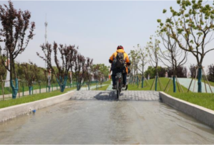 Rider cycling out of water covered test track section, pedalling away from the camera