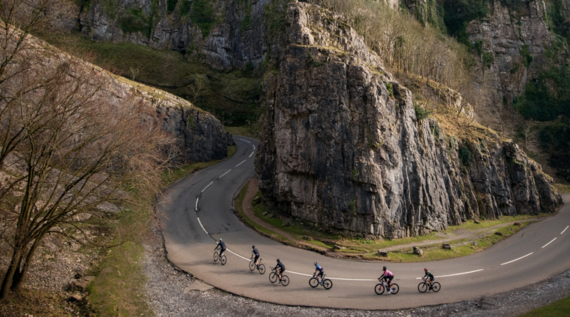 Long panoramic shot of cyclists ride around the bend in Cheddar Gorge