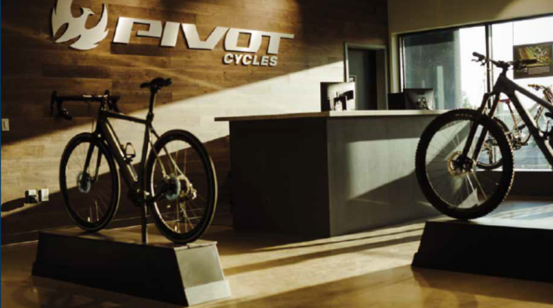 Pivot Cycles showroom - brand logo on far wall, two bikes on plinths, sunlight streaming on frmo the right side of the shot