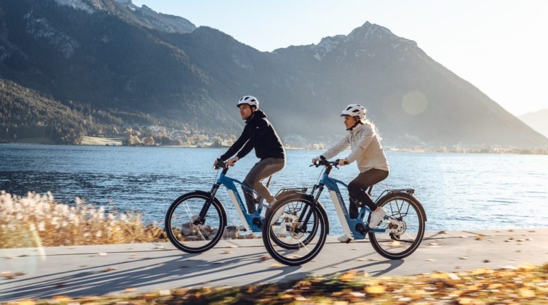 Advanced technologies Man and woman riding bikes along a lake with mountains in the background