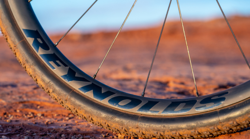 Reynolds Gravel rim with logo showing, tyre sitting on red gravel with blue sky in top of frame