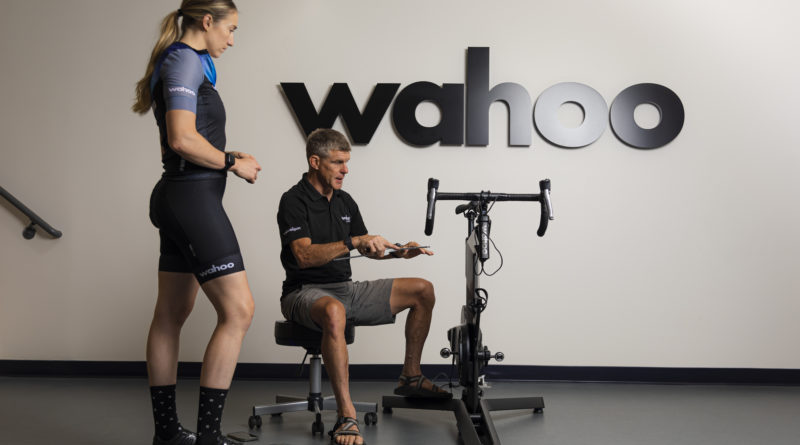 Women athlete stood next to Wahoo Kickr bike with man sat explaining adjustments to position