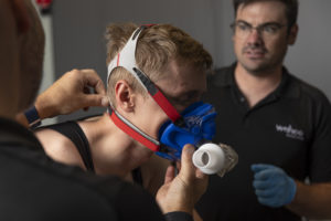 Male athlete getting ready for a Vo2Max test, with mask being fitted whilst sitting on static bike