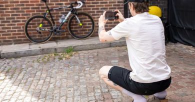 Rider squats across from bike lent against wall, mobile phone in hand, using the Apidura sizing tool app