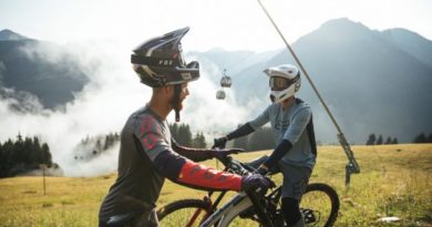 2 rides, helmets tilted back on tops of heads, stood with MTB, with chair lift in background
