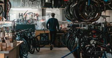Workshop scene with bikes hung on right in large numbers with workbench at the back or the shot