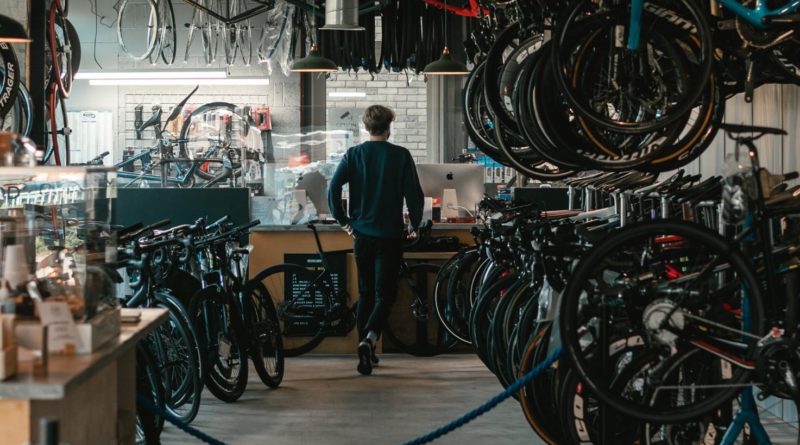 Workshop scene with bikes hung on right in large numbers with workbench at the back or the shot
