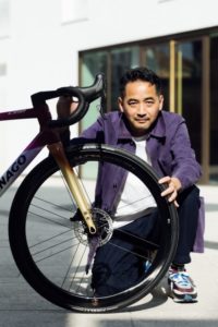 Motoki Yoshio x Colnago with artist crouched and holding the handlebar at the front wheel of the bike