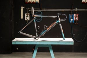 Frame, fork, seatpost and handlebar assembled and resting on bench in workspace