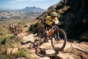 MTB rider pushing up rocky terrain with massive mountain vista in backdrop