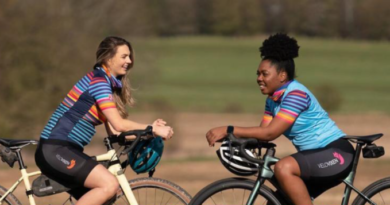 2 women facing each other sat on the top tubes of gravel bikes with a field as backdrop