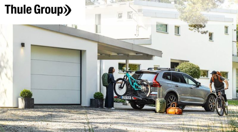 Thule Group logo over image of car with roof rail, bike rack on towing eye, one bike on and another cyclist riding past