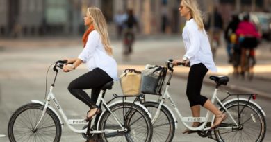 2 women riding bike share scheme bike in a city location