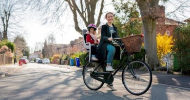 Mum and child on old style Dutch town bike, with child seat on back and basket on front. Picture taken on quiet, treee lined, urban residential road