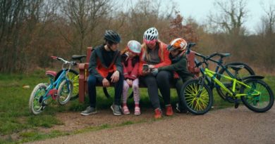 Woman and three children sat on park bench looking at mobile with bikes either side of them