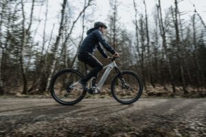 Porsche eBike Performance test mull being ridden with development motor on flat gravel path with light wood behind