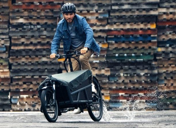 Man riding Riese and Muller cargo bike with wall of wooden cargo pallets in background