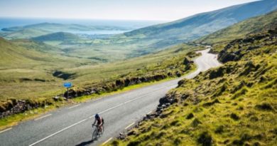 Cyclist riding up sun soaked Scottish highlands climb with green lowland hills in backdrop