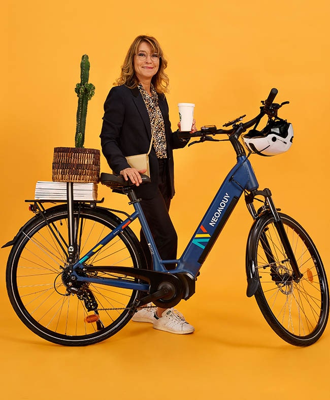 Woman holding urban eBike with books on rear rack and coffee in hand. Studio shot with yellow background