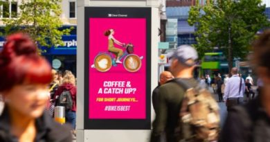 Digital billboard on highstreet with people walking up and down. 'Coffee and a catch up? slogan with digital cartoon of person riding bike with late art wheels