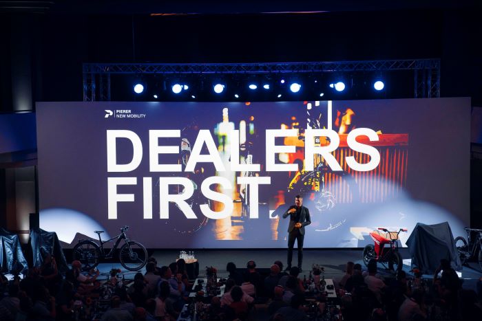 Pierer New Mobility pre Eurobike event 'Dealers First' - picutre looking over crowd, toward stage with #Dealers First' text on screen behind presenter
