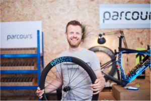 Dov Tate, Parcours founder, stood with wheel in hand and bike in background of branded display area