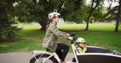 Women on eCargo bike with child sat in front. Riding through park space with trees and grass in background