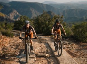 Ciovita Women's team, Elrika Harmzen and Jessica Wilkinson riding a dustry trail on the 2023 edition of the Trans Baviaans MTB race with mountains in the background