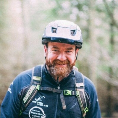 Graeme McLean. Profile picture. Dressed in MTB helmet and rucksack, stood trail side.