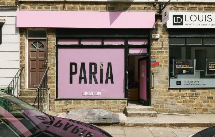 Paria cafe front with branding on window and above. Pink with black letters. Image taken from across the street