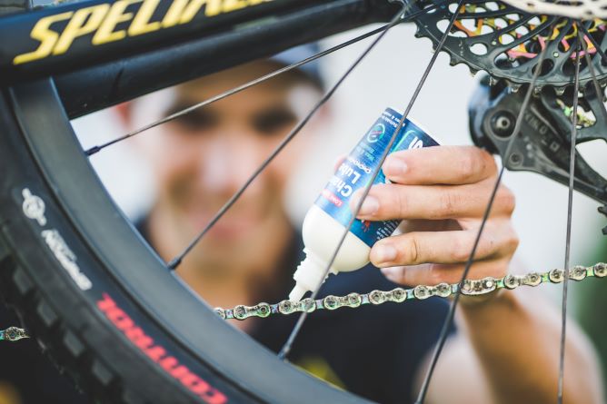 Close up of man applying Squirt lube to his mountain bike chain. Picture taken looking through the no drive side of the rear wheel