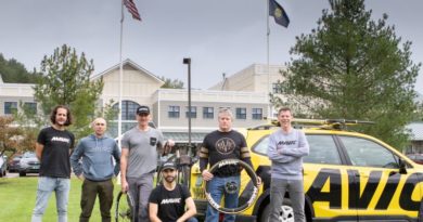 Mavic North American team, Benjamin Grenon, Fabrice Gaydon, Guenter Hofer, Josh Saxe, Scott Bergin, and Lionel Kamard stood in front of building with state and national flags flying