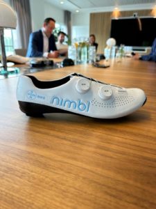 Nimbl shoe with Pon Bike logo on outside of heal cup, resting on boardroom table with people in the backdrop, out of focus