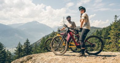 Man and woman on eMTB at peak of trail head with mountains and forest in backdrop
