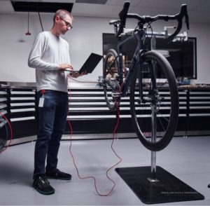 Specialized Roubaix in workstand with telemetry sensors connected to laptop being held by tall man in glasses