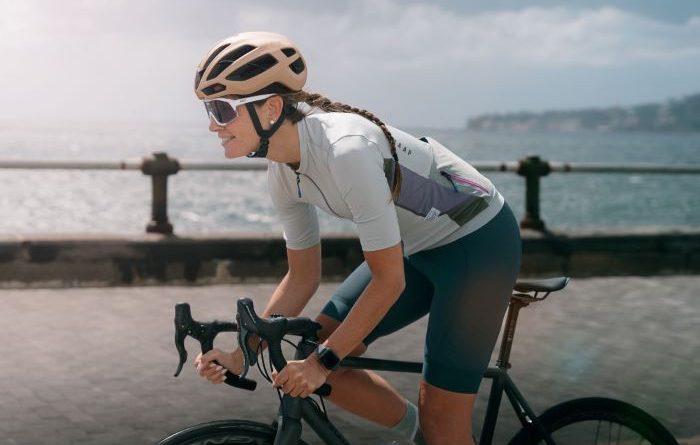 Women rider in Kask Protone helmet, on road bike, cycling along promenade with sea in the background.