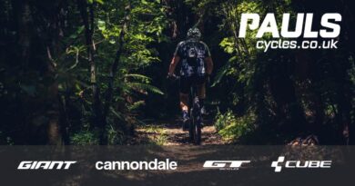 Mountain bikers riding on woodland trail. Image overlay with Paul's Cycles name and that of bike brand partners