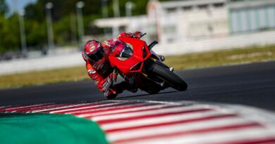 Ducati motorcycle on race track, with ride 'knee down' mid corner. Photo taken from on front, looking back at the bike